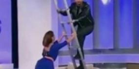 بالفيديو.. مذيع يسقط من أعلى سلم حديدي على الهواء ويقع على زميلته