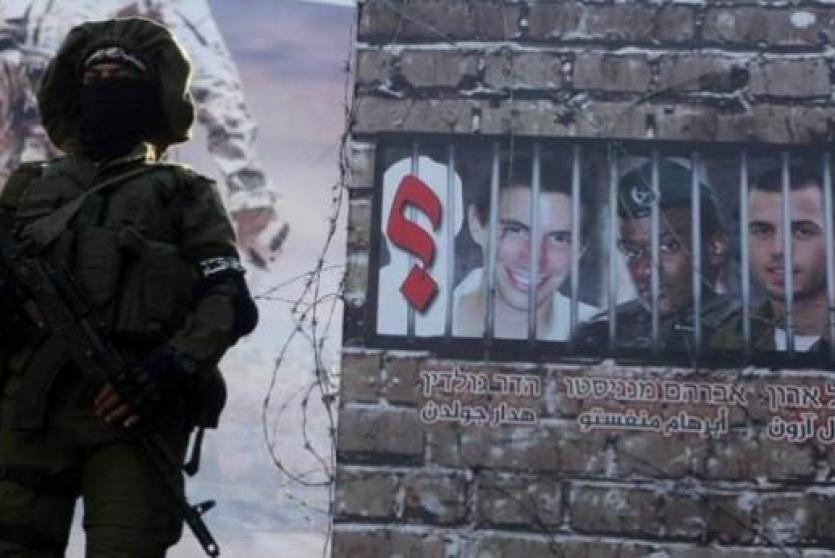 عنصر من القسام يقف بجانب صورة للجنود الإسرائيليين المفقودين في غزة  