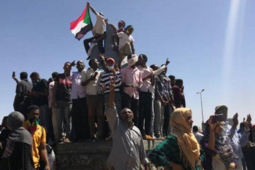متظاهرون يلوحون بالعلم السوداني أمام مقر الجيش في السادس من إبريل/نيسان