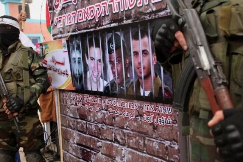 عنصران من القسام أمام مجسم وضعت عليه صور الجنود الاسرى