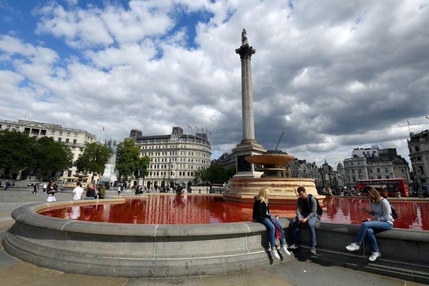 أناس يجلسون قرب نافورة في لندن سكب فيها محتجون صبغة حمراء