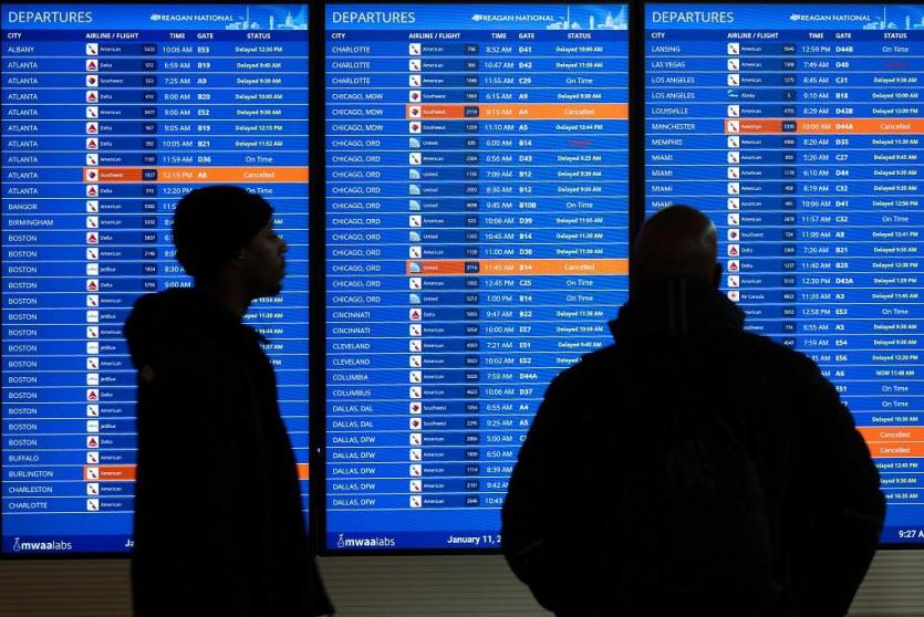 مسافران ينظران إلى لوحة عرض الرحلات المتأخرة والملغاة في مطار رونالد ريغان الوطني